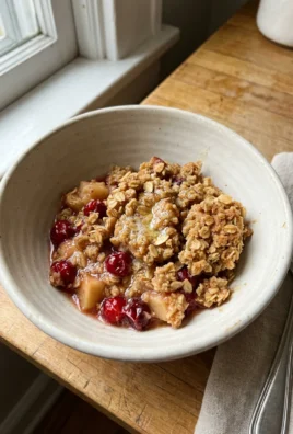 A single serving of apple cranberry crisp topped with a scoop of melting vanilla ice cream.