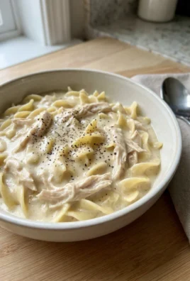 A close-up of a white bowl filled with creamy chicken and wide egg noodles.
