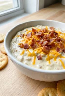 A close-up shot of a bowl of creamy chicken ranch dip topped with bacon.