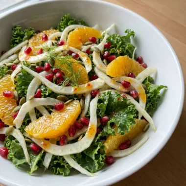 A fork taking a bite of fennel and pomegranate salad from a white plate.
