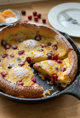 A top-down view of a golden brown, puffy pancake with cranberries in a cast-iron pan.