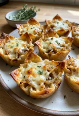 A single French onion phyllo cup held between two fingers, showing the layers of filling and cheese.