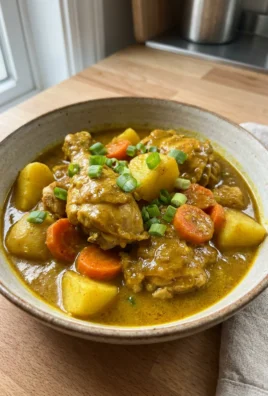 A close-up shot of a bowl of Jamaican curry chicken garnished with fresh herbs.