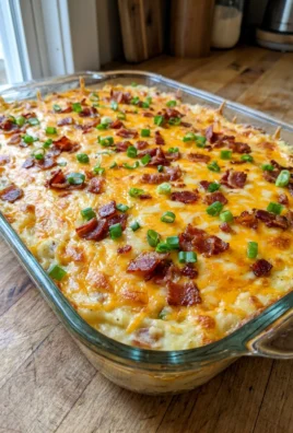 A large spoon scooping a serving of cheesy mashed potato casserole from the dish.