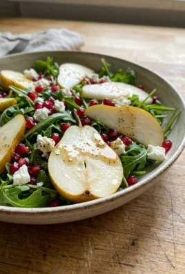 A bright and colorful arugula salad with sliced pears and red pomegranate seeds.