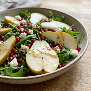 A bright and colorful arugula salad with sliced pears and red pomegranate seeds.