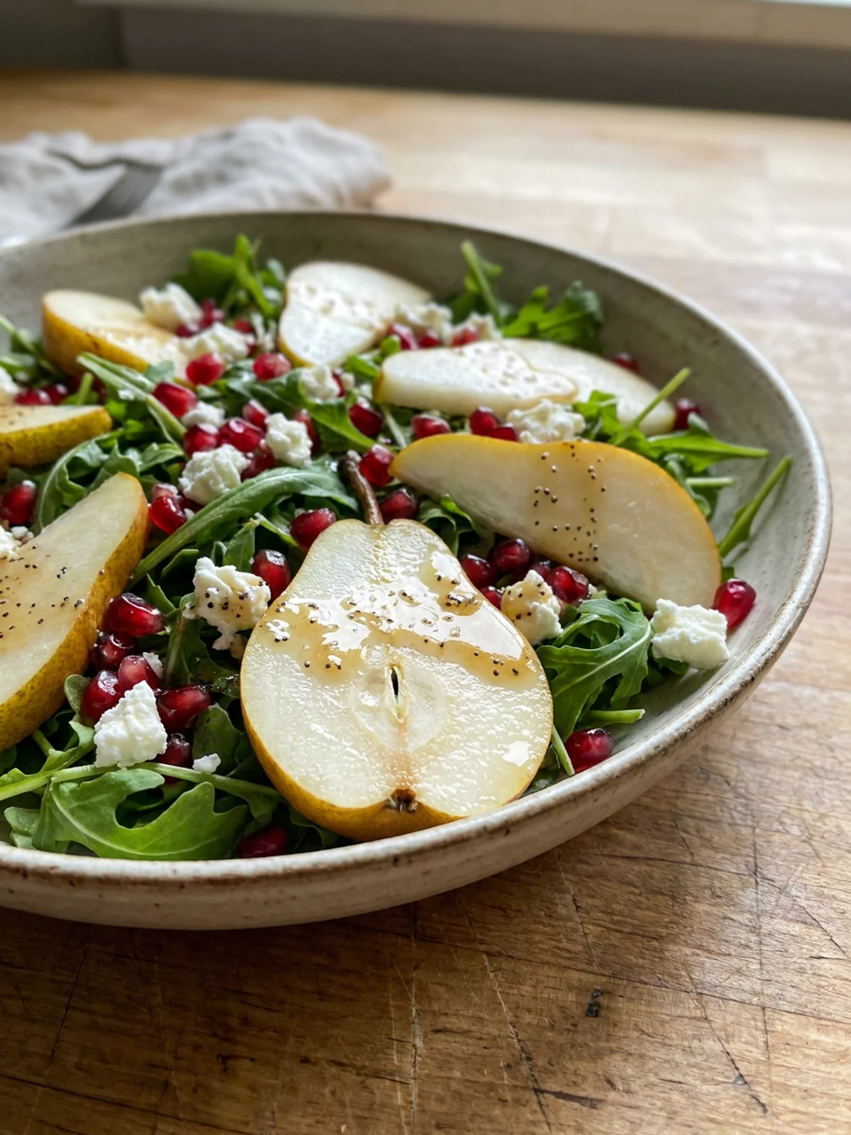 A bright and colorful arugula salad with sliced pears and red pomegranate seeds.