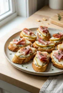 A close-up of a single pear and prosciutto crostini on a white plate.
