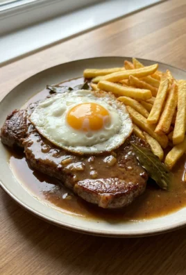 A close-up of a steak topped with a runny yolk egg and a glossy sauce.