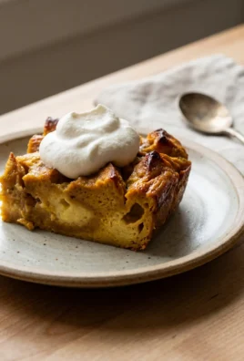 A square slice of pumpkin bread pudding topped with whipped cream on a small plate.