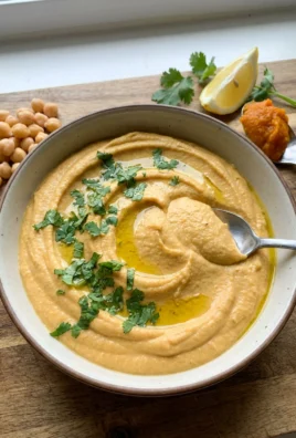 A close-up of a ceramic bowl filled with creamy pumpkin hummus with a swirl on top.