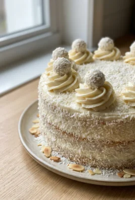A whole Raffaello cake on a white plate against a clean background.
