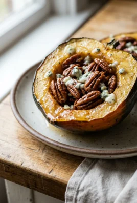A close-up of a roasted acorn squash with maple pecans on a white plate.