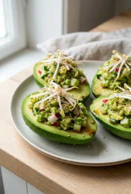 A top-down view of several stuffed avocados garnished with fresh sprouts and seeds.