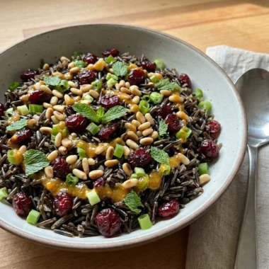 A spoonful of wild rice salad with orange vinaigrette being lifted from a serving bowl.